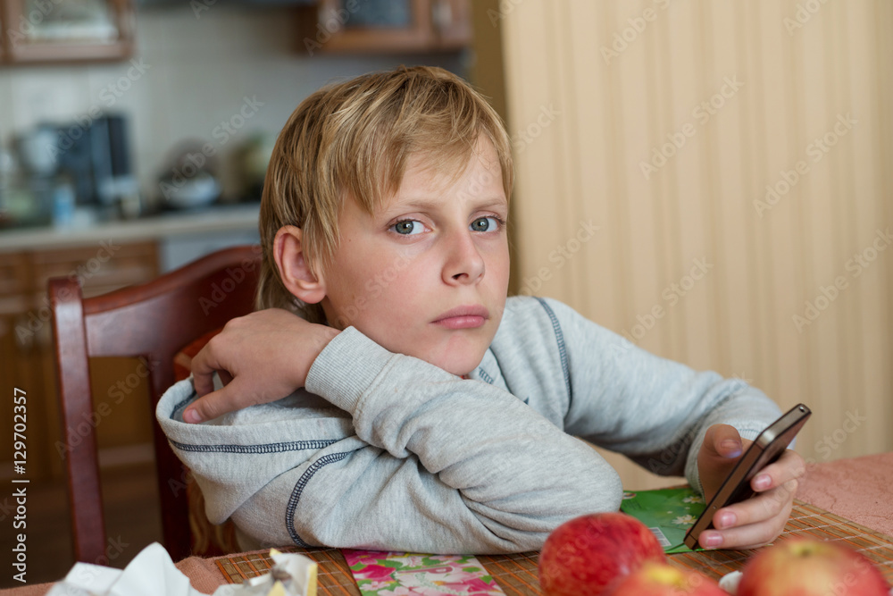 Naklejka premium Boy sitting at table at home with the phone