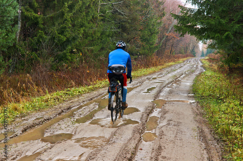 A cyclist on a wet road in the autumn forest. Puddles in the forest after the rain.