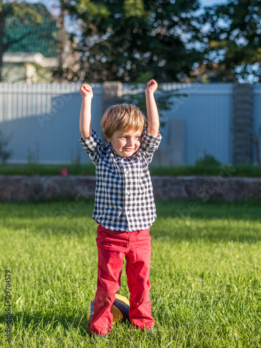 Happy child playing on the green grass, dressed in a plaid shirt and red pants