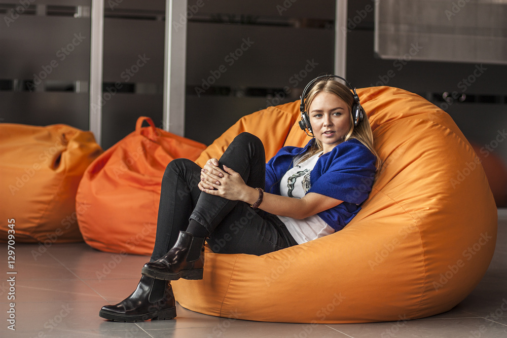 Armchair traditional bean bag for fun and relaxation orange color. Young  woman with headphones while sitting on big cushioned frameless chair Photos  | Adobe Stock