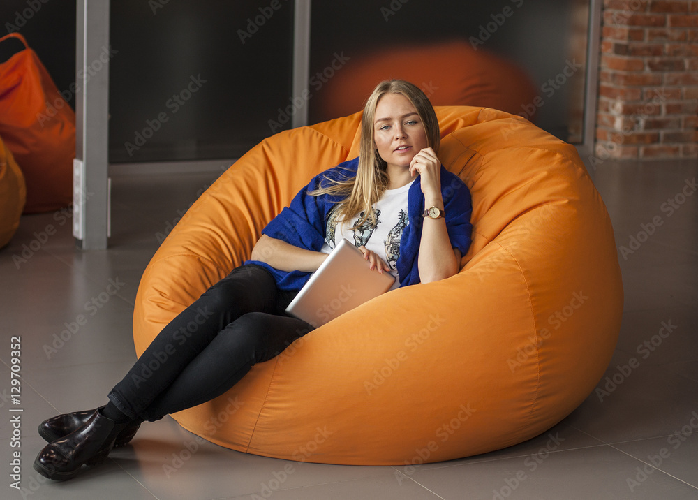 Armchair traditional bean bag for fun and relaxation orange color. Young  woman using tablet screen while sitting on big cushioned frameless chair  Stock Photo | Adobe Stock