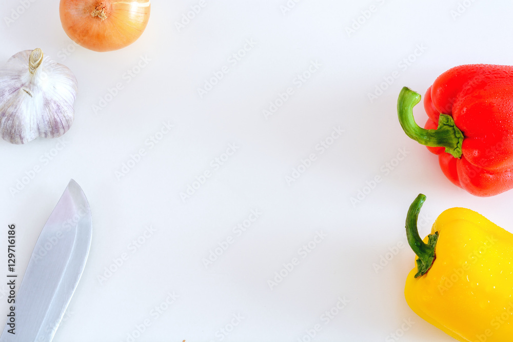 Red and yellow peppers, onion, garlic and knife on a white background, top view