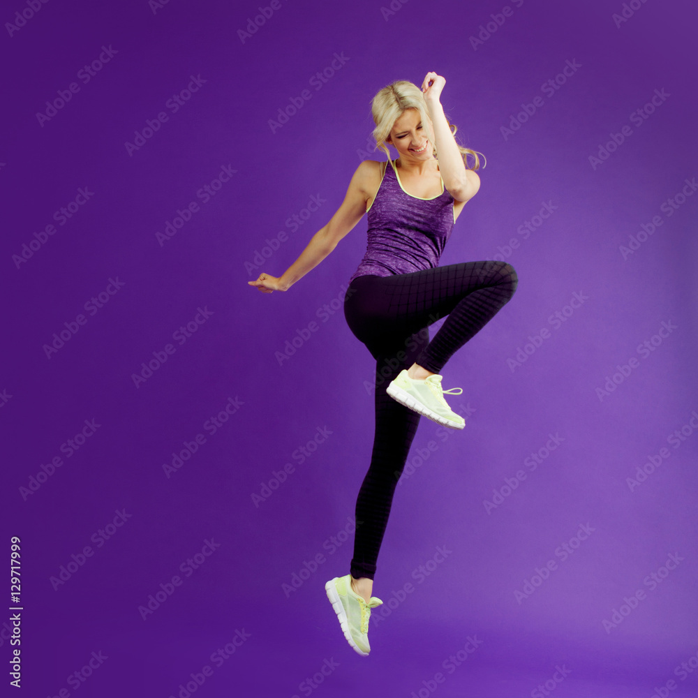 Obraz premium Beautiful young girl in a pose runner. Studio background, purple. Happy jumping