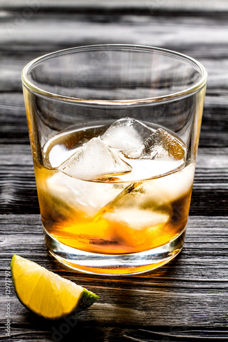 rum with ice in glass on dark background and lime