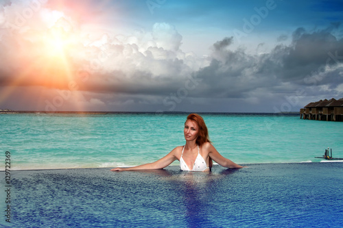 The young beautiful woman in the pool before the sea at sunset
