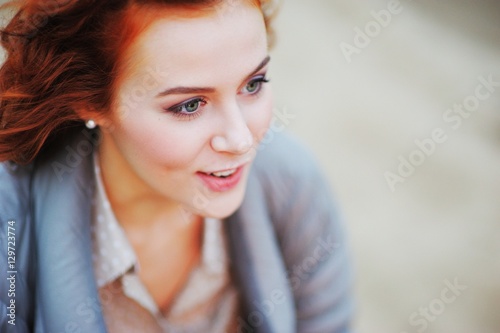 Portrait of young beautiful surprised smiling girl with red-brown hair in a gray jacket outdoors on blurred background, close-up.