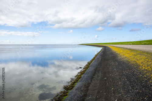 shoreline of Ameland Island  with view over the wadden sea  with clouds reflecting in water at dawn and a bike lane over a dike