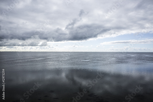 shoreline of Ameland Island, with view over the wadden sea, with clouds and tourmented sky reflecting in water at dawn