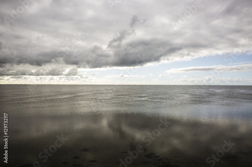 shoreline of Ameland Island  with view over the wadden sea  with clouds and tourmented sky reflecting in water at dawn