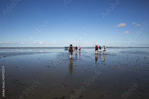 Maritime landscape with reflection of clouds in low tide water and group of people trekking, Waddenzee, Friesland, The Netherlands