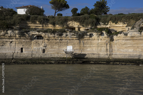 View from the Gironde estuary with the limestone cliff of the village of Meschers sur Gironde and its troglodytic houses and traditionnal typical wooden fisherman cabin, Charente maritime, France photo