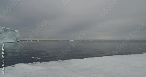 Scenic pan left of ice cliff above calm arctic sea photo