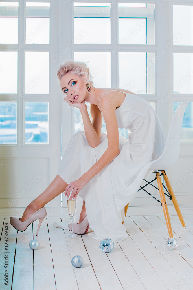 Beautiful blond woman in a long dress sitting on a chair in the Beautiful blond woman in a long dress sitting on a chair in the