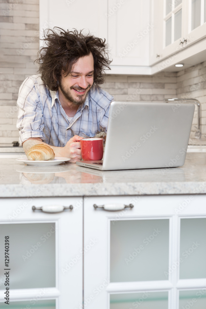 Fototapeta premium Man Eating Breakfast Using Laptop, Man in kitchen drinking coff