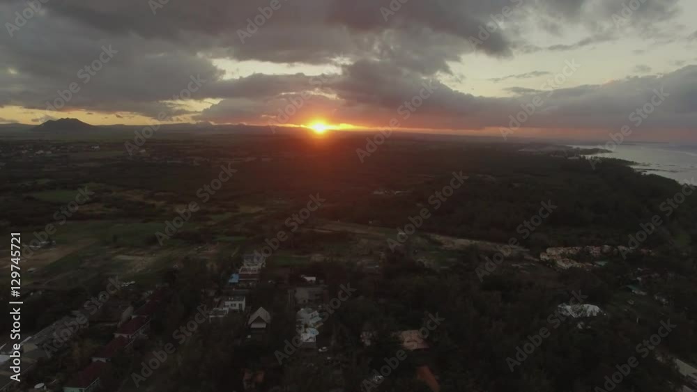 Flying over town and vast green forested areas on Mauritius Island at sunset in cloudy sky Flying over town and vast green forested areas on Mauritius Island at sunset in cloudy sky