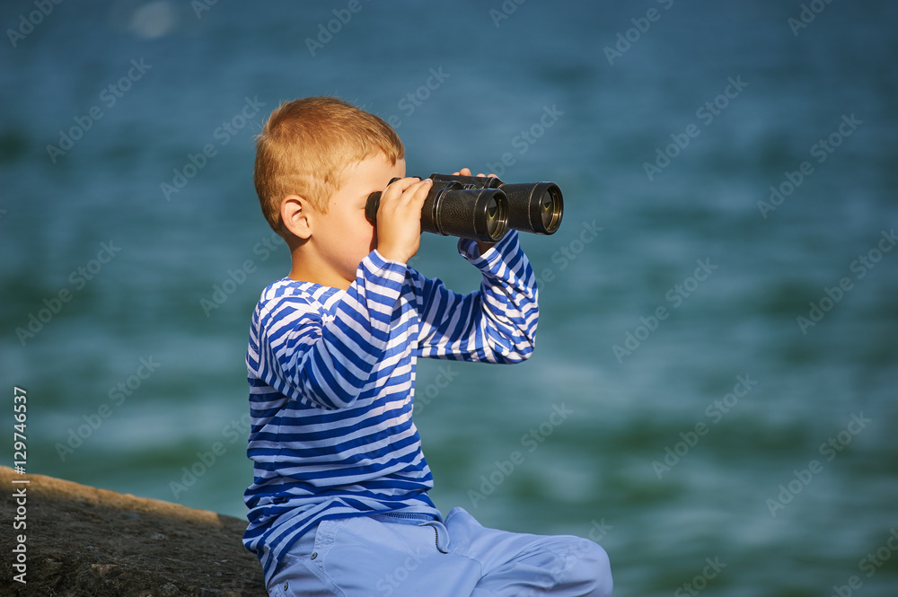 little boy with binoculars , the sea in the background