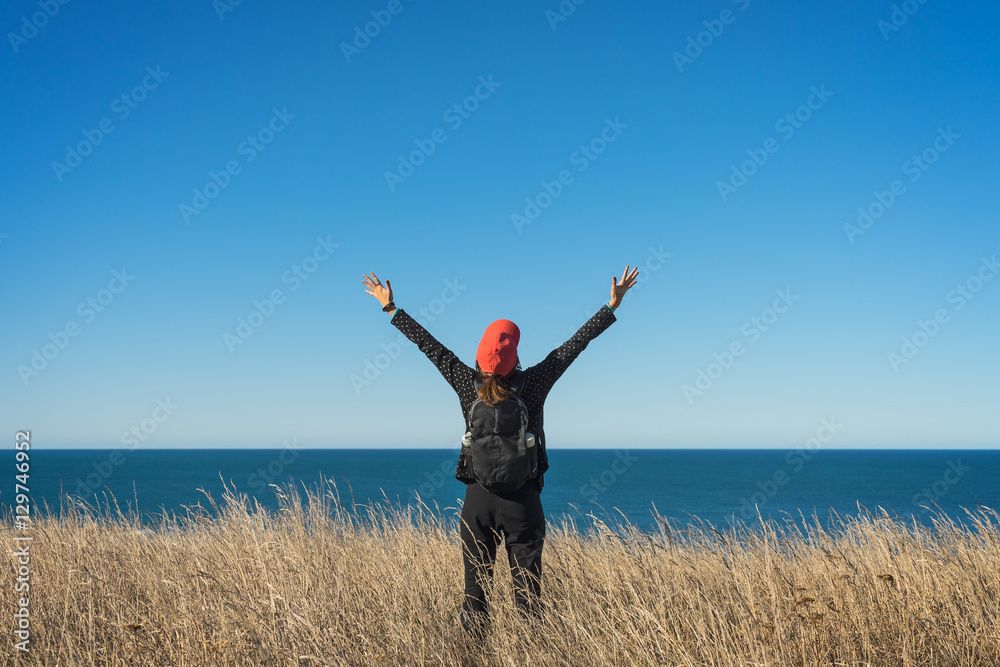 Woman tourist standing on meadow with ocean view Woman tourist standing on meadow with ocean view