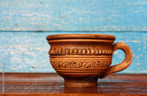 Clay brown mug with ornament pattern on a blue wooden background. Ukraine