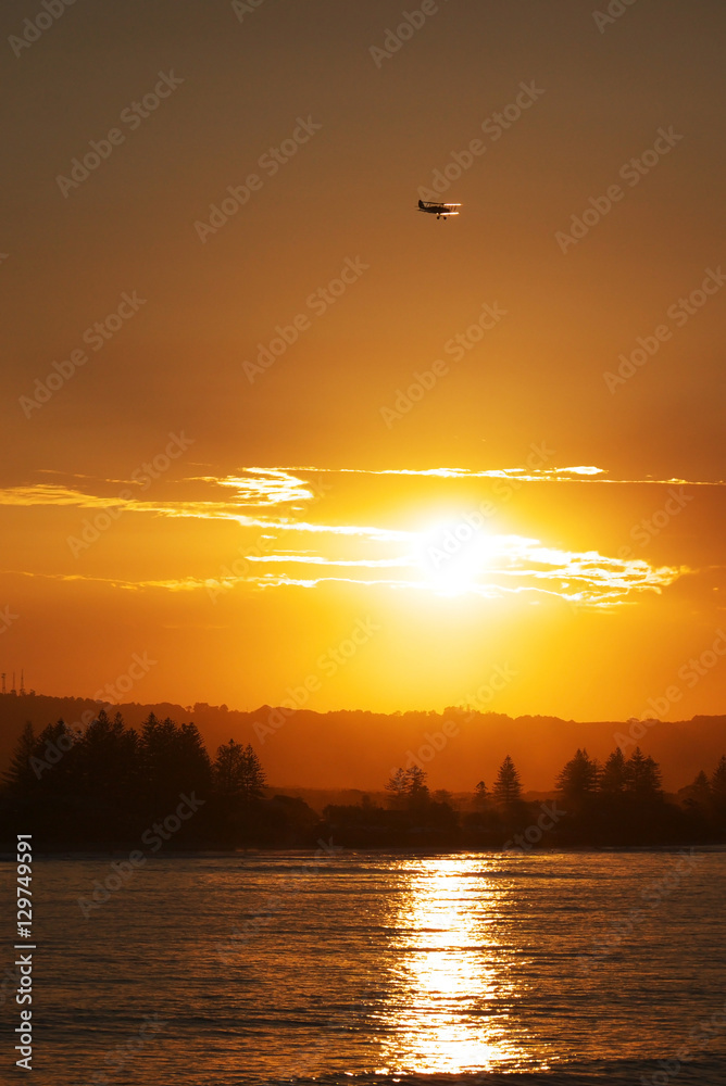 Flugzeug fliegt bei Sonnenuntergang über die Küste