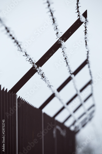 High fence and barbed wire with ice crystals