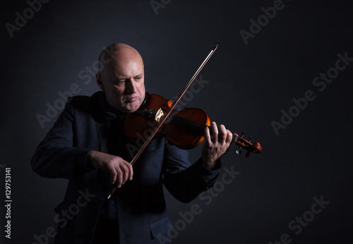 A man passionately playing the violin on dark background.