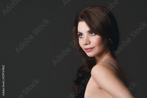Beautiful sexy girl wearing black evening dress on a gray background. Brunette with charming smile and an open dress