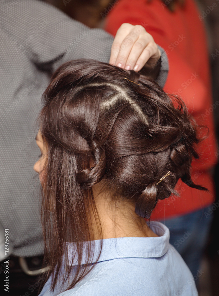 Naklejka premium Hairdresser curling woman hair with electric iron curler tong. Hairstylist making woman hairstyle.