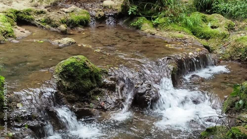 Small waterfall in forest. Pure fresh water waterfall. Water runs over stones covered with moss Small waterfall in forest. Pure fresh water waterfall. Water runs over stones covered with moss