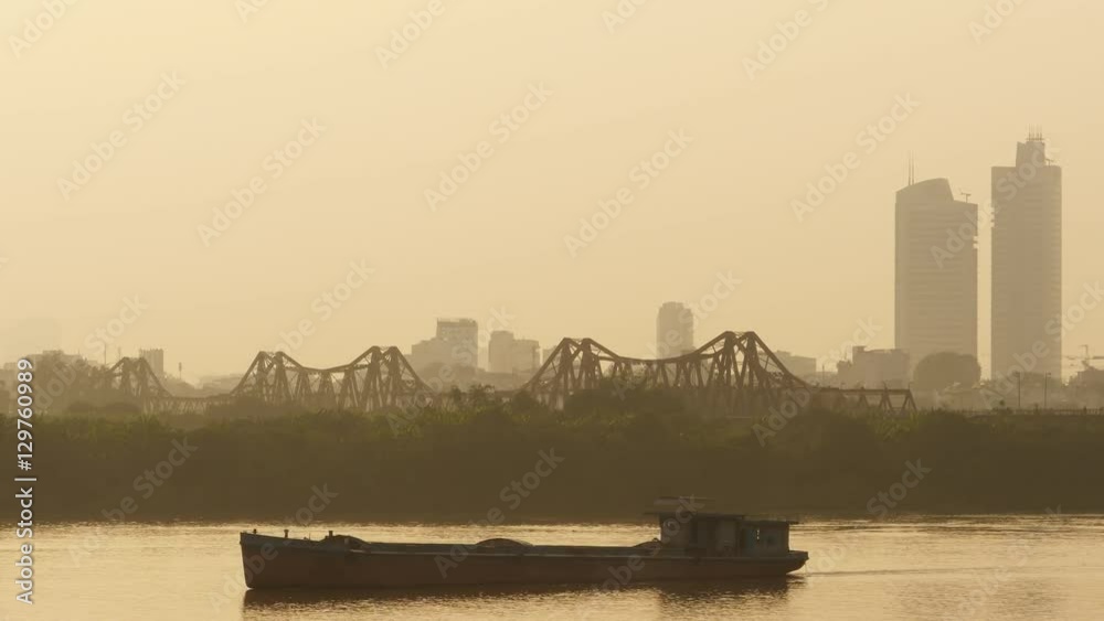 Hanoi city in the evening haze with a passing cargo ship. Overlooking the river.