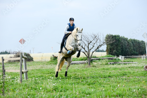 beautiful young woman riding horse and training for jump hurdle equitation competition outdoor