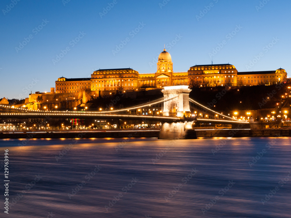 Illuminated Buda Castle and Chain Bridge over Danube River in Budapest by night, Hungary, Europe. UNESCO World Heritage Site. Long exposure shot with blurred water stream.