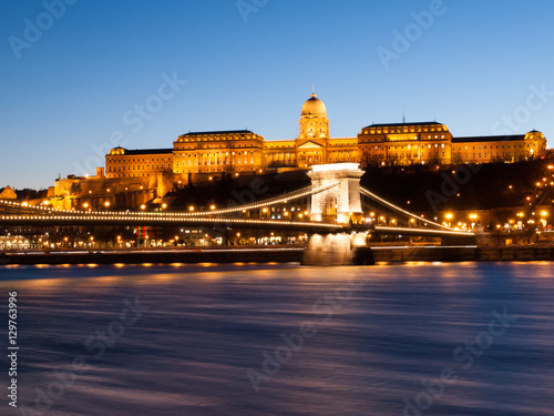 Illuminated Buda Castle and Chain Bridge over Danube River in Budapest by night, Hungary, Europe. UNESCO World Heritage Site. Long exposure shot with blurred water stream.