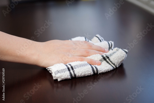 Young woman hand cleaning modern wood table by dust cloth (color
