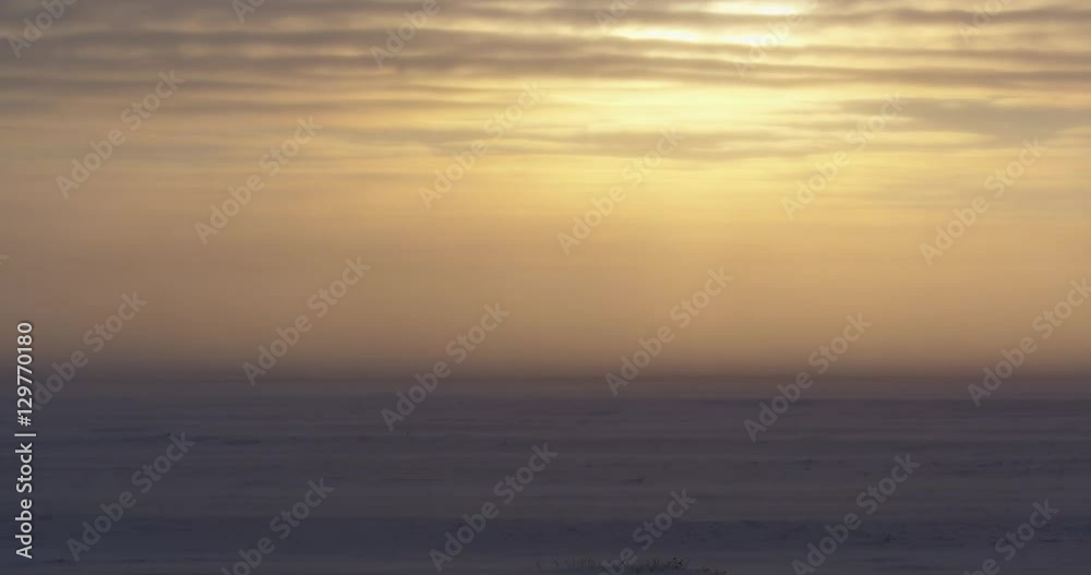 Empty tundra in sunset blizzard with sun ice and blowing snow