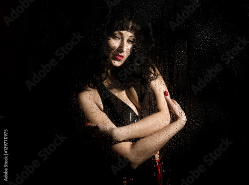 black widow in a veil, mysterious sad woman wearing lace. posing behind transparent glass covered by water drops