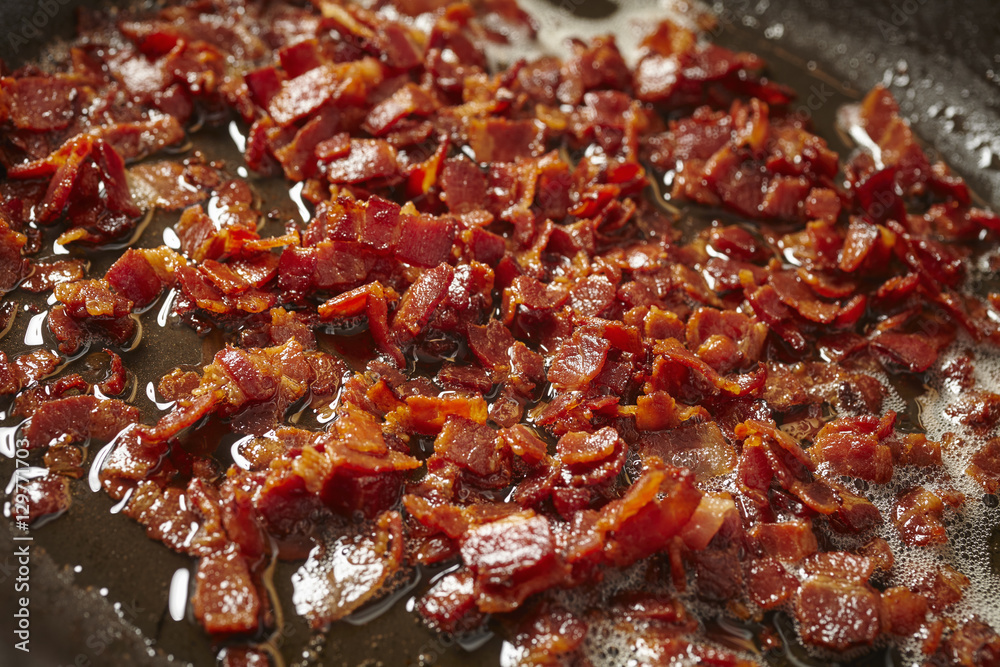 pieces of bacon frying in a skillet pieces of bacon frying in a skillet