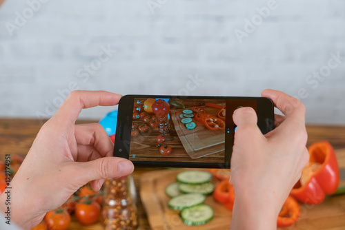 Young woman cooking and taking photo of vegetables by smartphone
