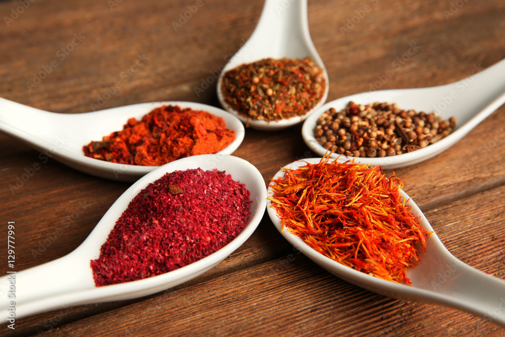 Spices in spoons on a wooden background