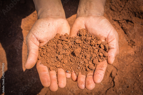Red and dry soil on the hands in the drought land.