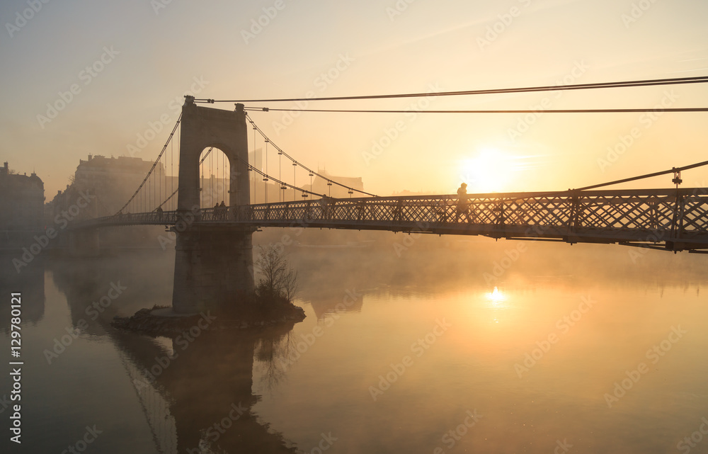 Obraz premium Pedesrtians on the monumental Passerelle du College bridge over the Rhone river in Lyon on a foggy morning.