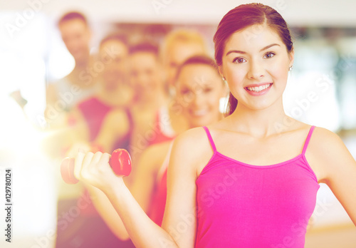 group of smiling people with dumbbells in the gym