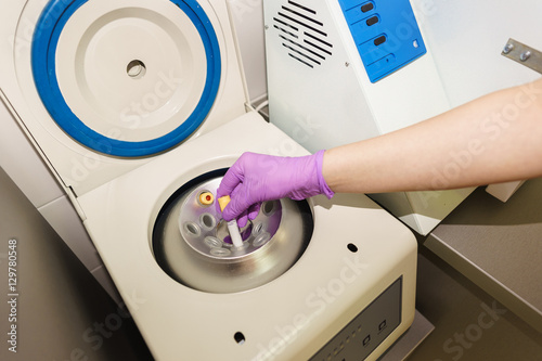 A gloved hand places the vial in the slot tabletop