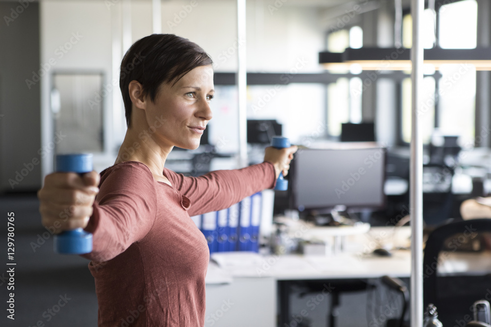 Businesswoman in office exercising with dumbbells Businesswoman in office exercising with dumbbells