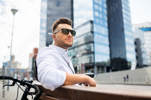 happy young man with bicycle sitting on city bench