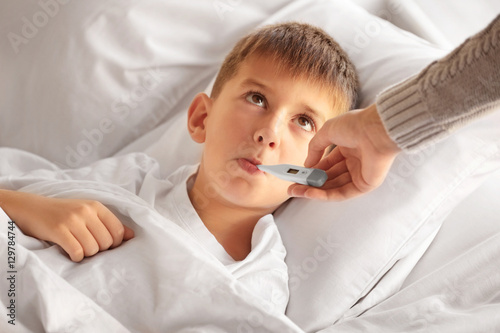 Small sick boy with thermometer in bed