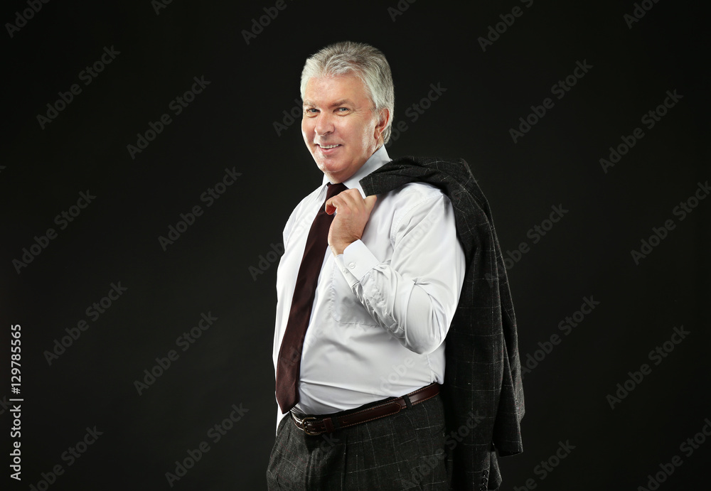 Senior businessman holding jacket on black background