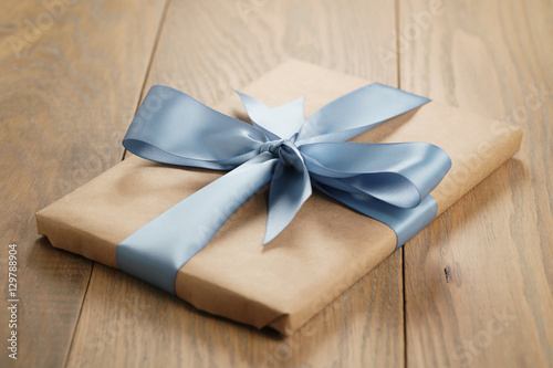 handmade gift brown paper box with blue ribbon bow on wood table, shallow focus