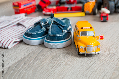 School bus toy near shirts and blue boat shoes on grey wooden background. Boy outfit. Close up.