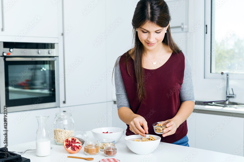 Beautiful young woman preparing cereal bowls in the kitchen.