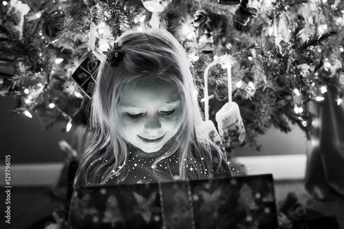 Bild auf Leinwand young girl opening magical present under the christmas tree